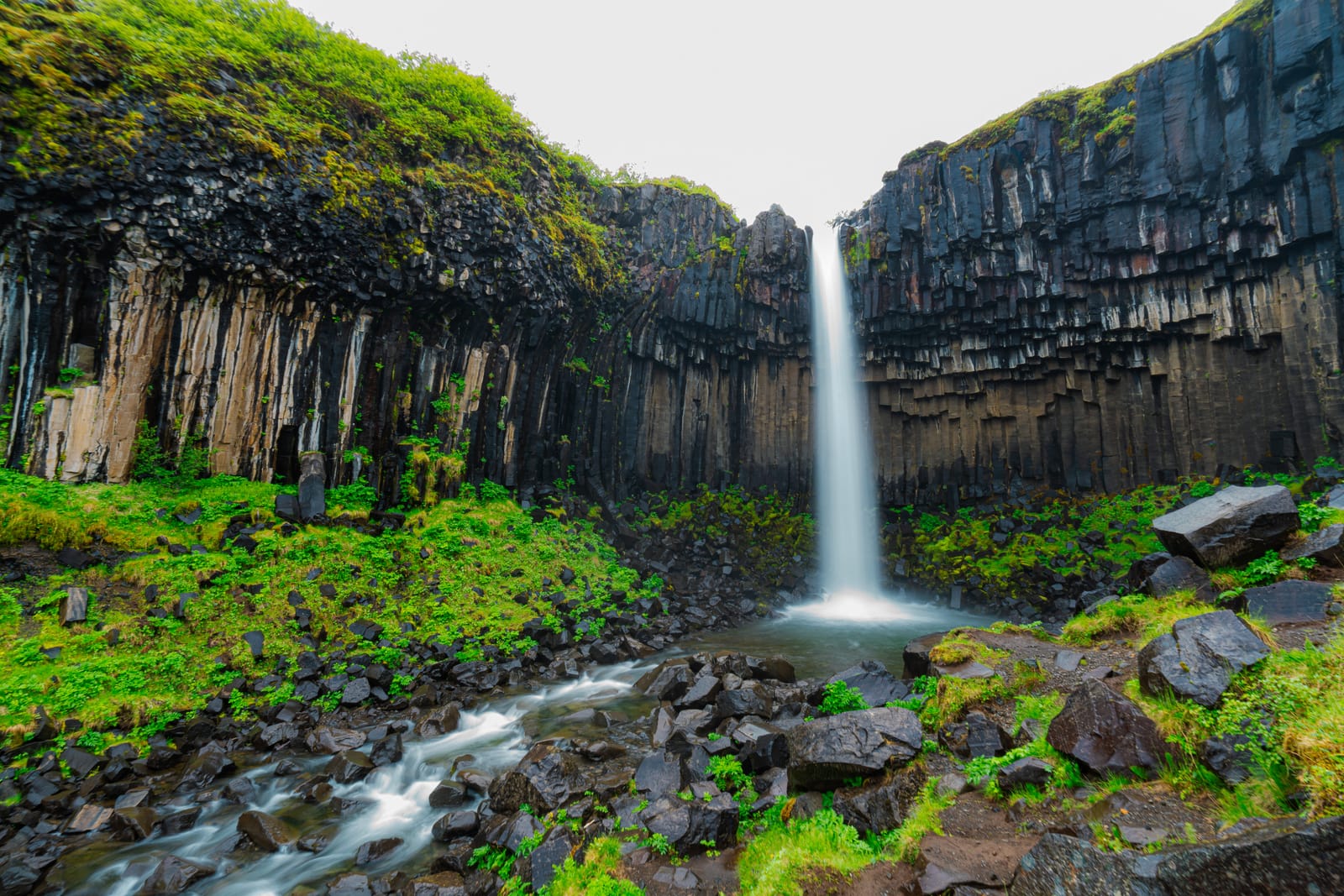 Waterfall over basalt columns, green moss.